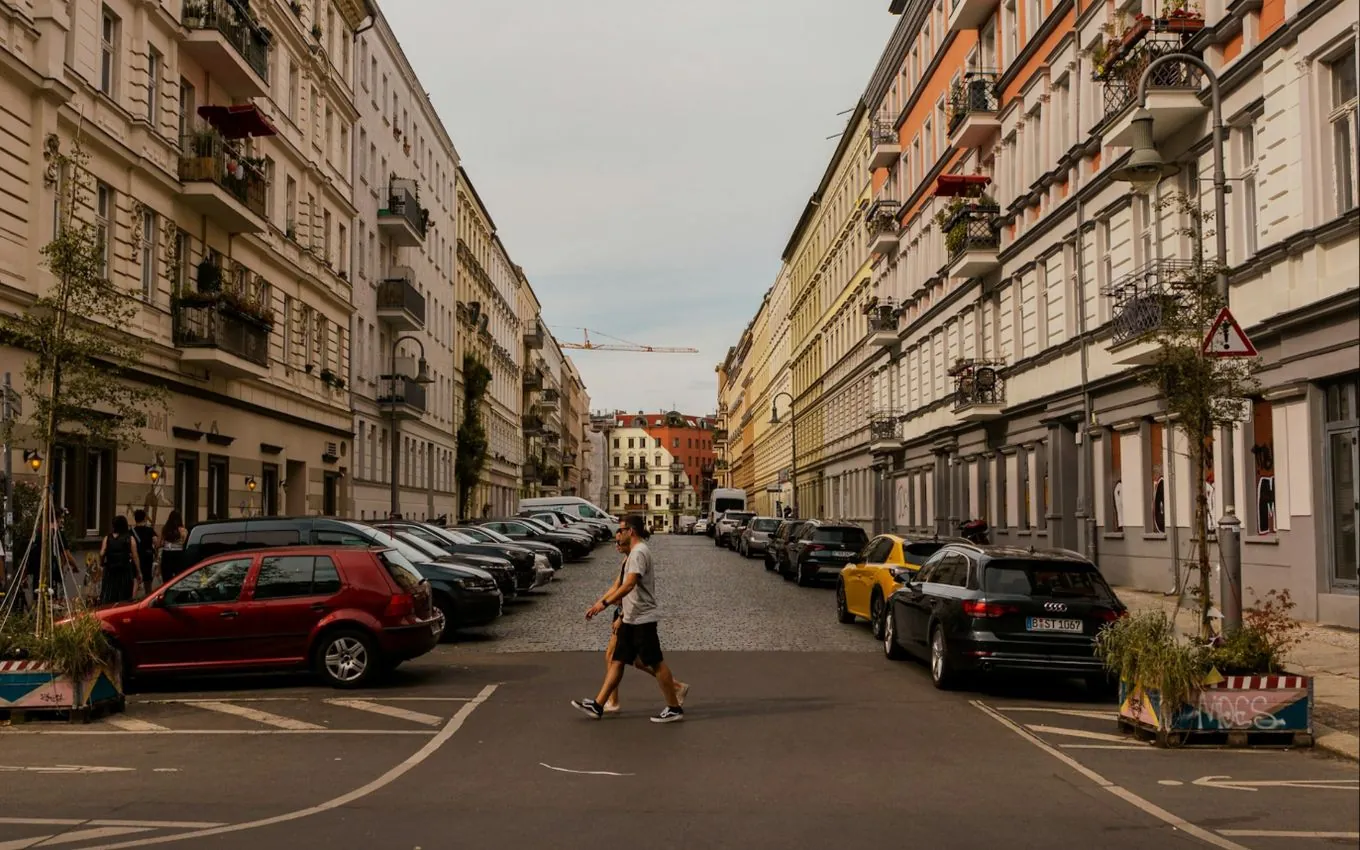 A Berlin side street with Altbau façades, parked cars and a man crossing the road