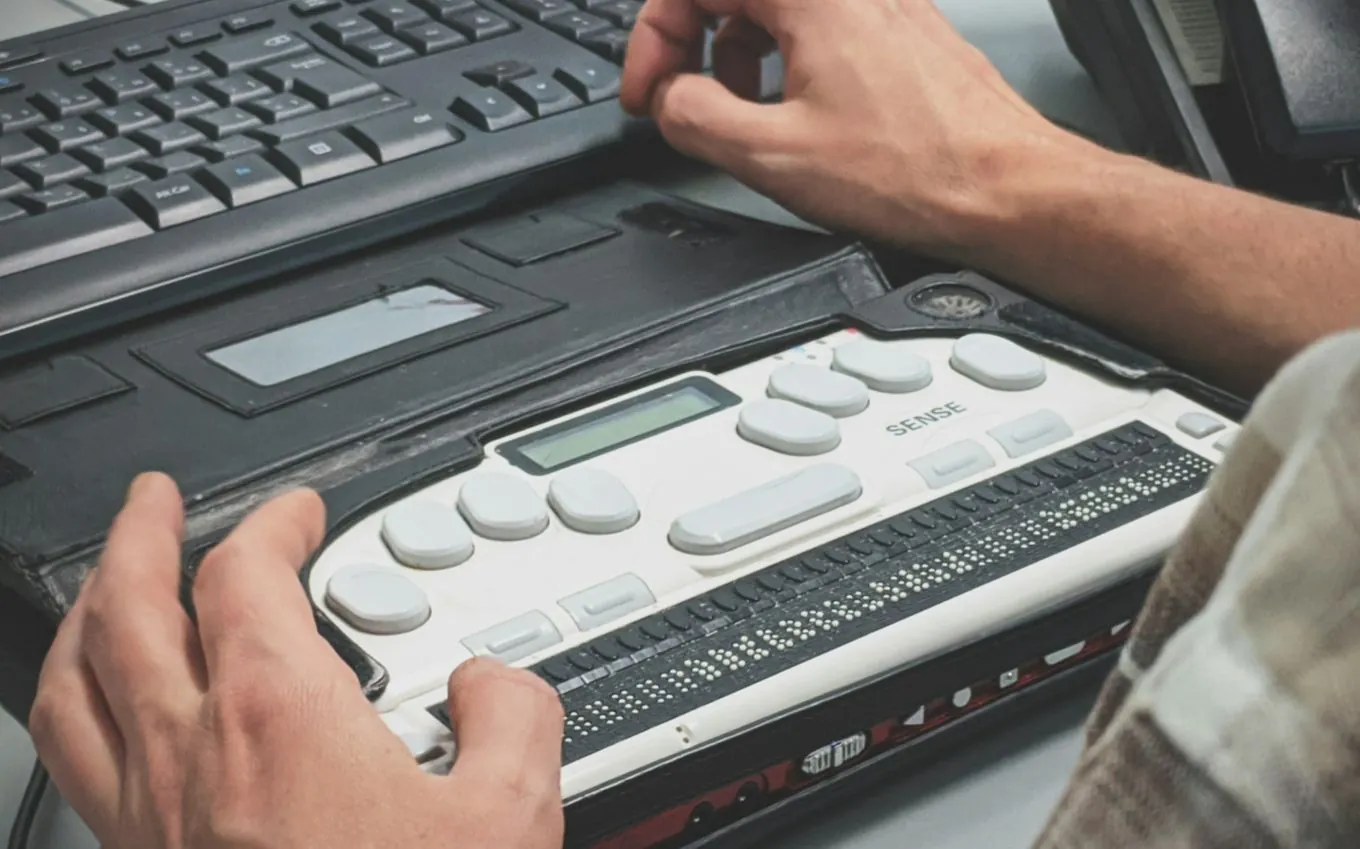 Hands on a refreshable braille display in front of a keyboard