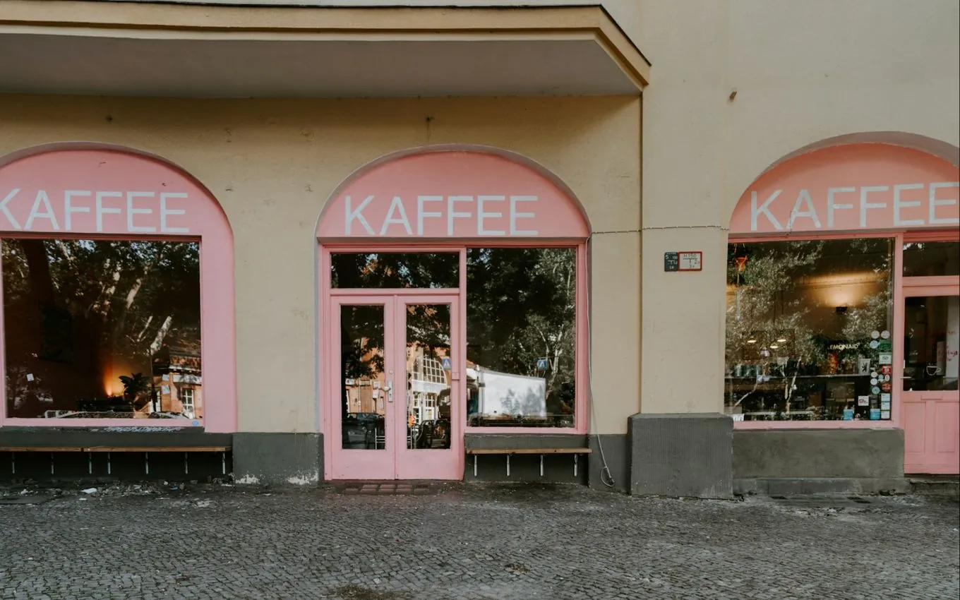 A café front with three arched windows, pink frames and the word KAFFEE painted above each window