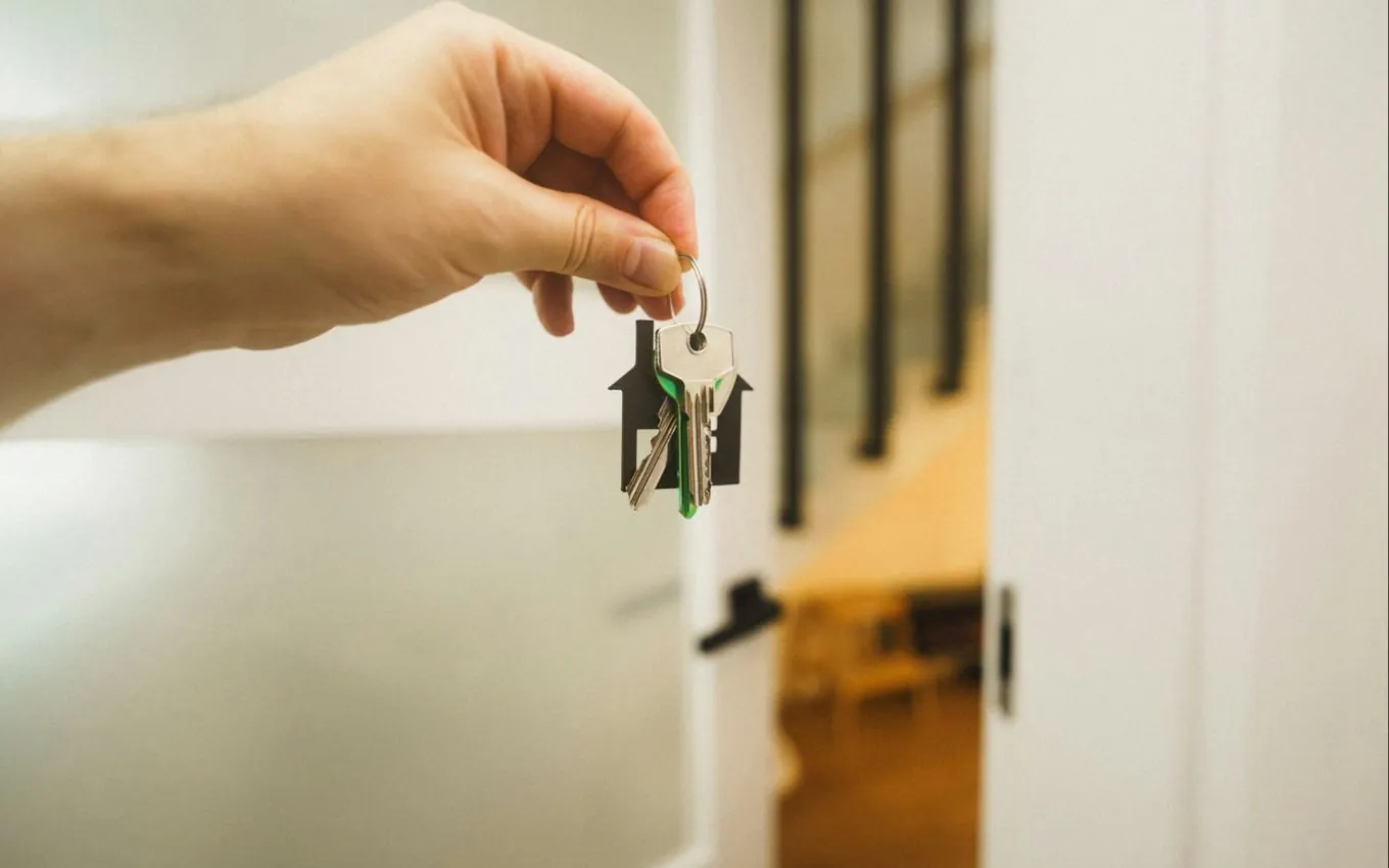 A hand holding a bunch of keys on a house-shaped keyring in front of an open apartment door