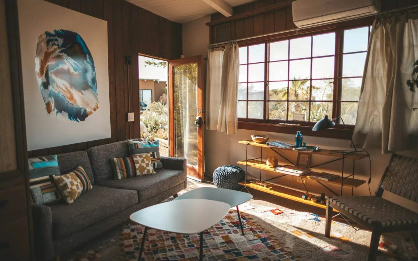 A sunlit living room with a grey sofa, patterned cushions, a rug and an open door to a garden