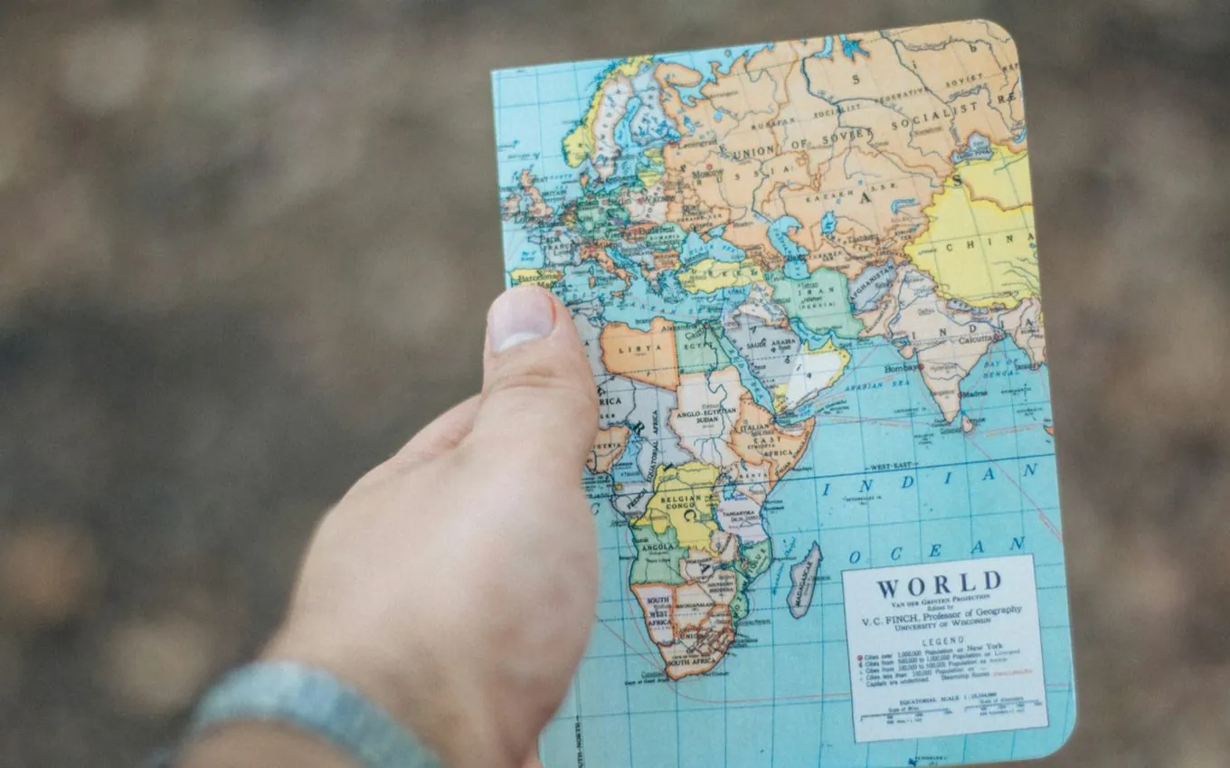 A hand holding a small world map notebook