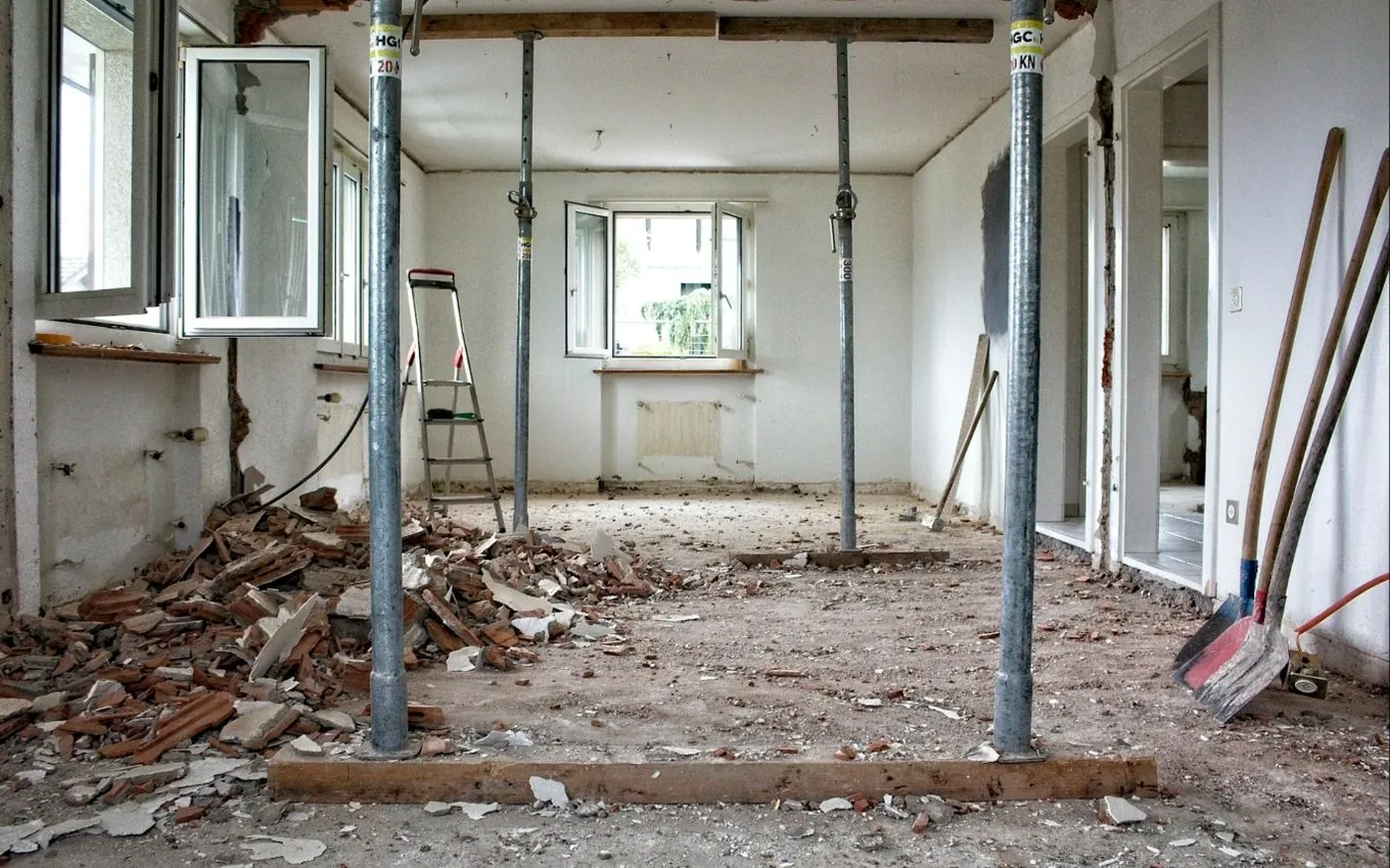 A gutted room under renovation, with steel props holding up the ceiling and rubble on the floor