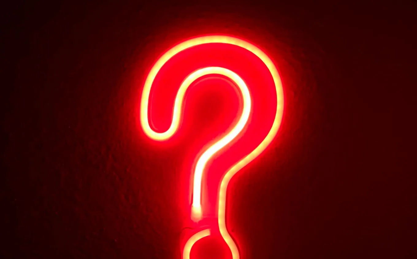 A red neon question mark on a dark wall