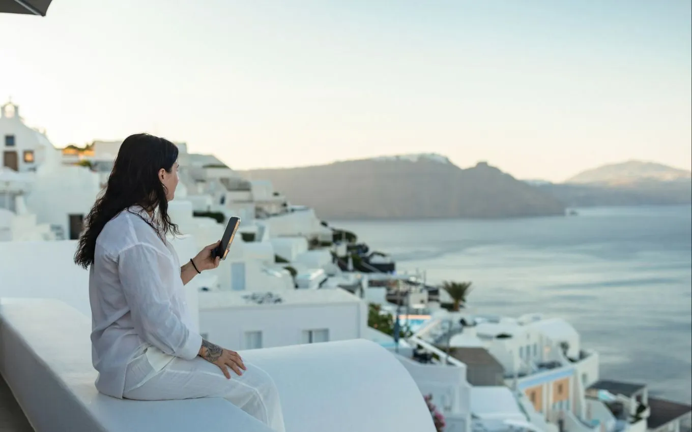 A woman with a phone on a white rooftop wall above the sea in Santorini