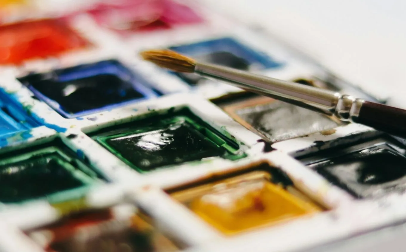 A watercolour box with a brush resting across the pans